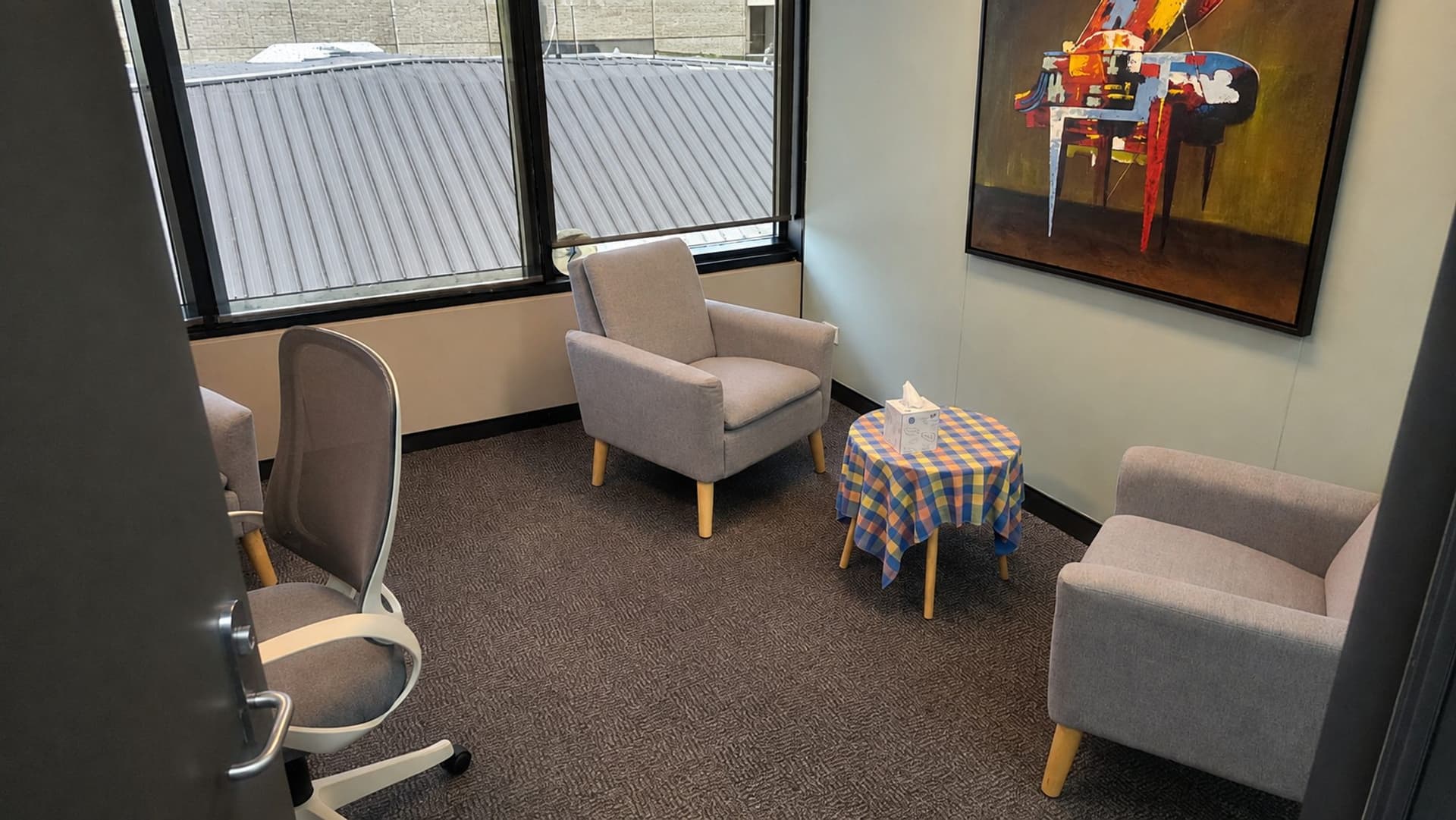 The counselling room at The Listening Room in Curtin: two soft armchairs facing each other, a small table with a box of tissues, and a window.